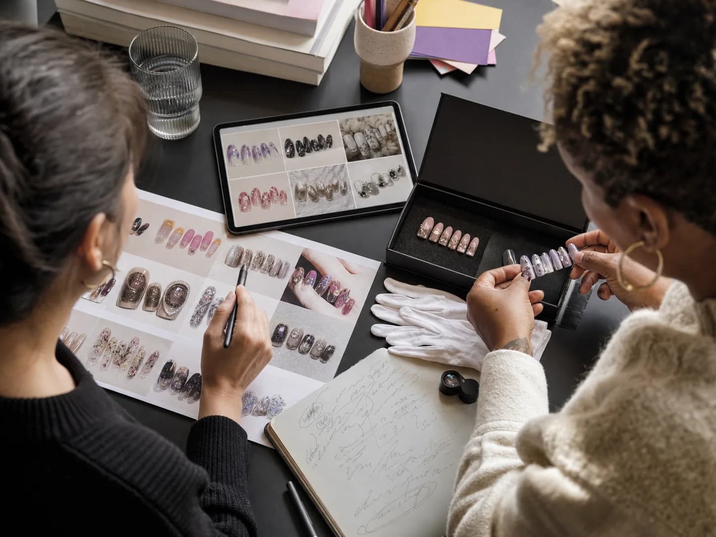 Two reviewers carefully comparing an artist portfolio with a physical press-on nail set